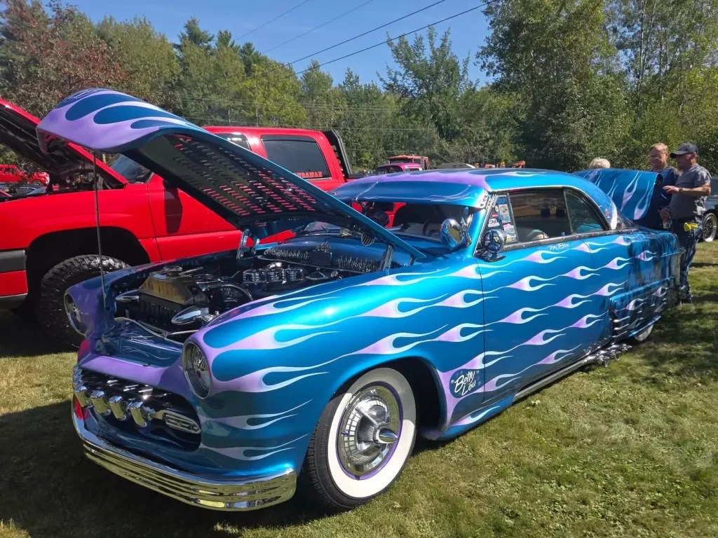 Blue custom Mercury coupe named Betty Lou with lavender flame graphics and its hood open at Freddie's Cruise-In 2026 in Vassalboro, Maine.